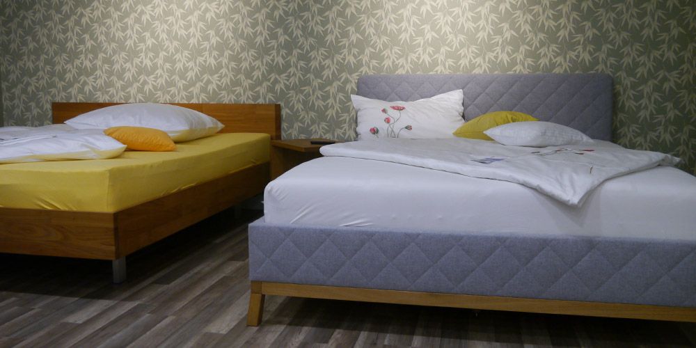 Zwei Betten mit freudiger Bettwäsche vor einer mit Blättern tapezierten Wand